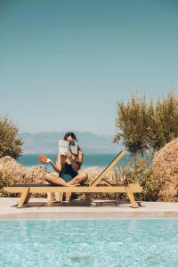 a woman sitting on a bench reading a book next to a pool at ​Le Grand Bleu Resort in Derveni