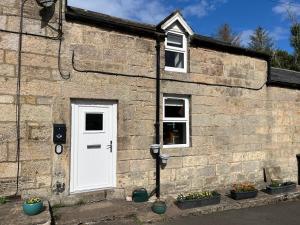 a brick building with a white door and windows at Cosy Northumberland Studio Cottage in Thropton