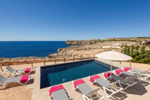 a swimming pool with chairs and an umbrella and the ocean at Villa Aguamarina by Villa Plus in Cala en Forcat