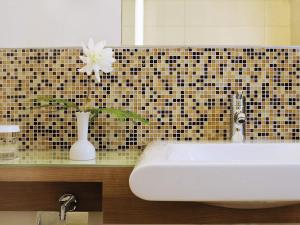a bathroom with a white sink and a vase with a flower at Mövenpick Hotel Zürich-Regensdorf in Regensdorf