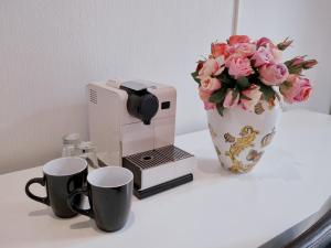 a coffee maker with two cups and a vase with pink roses at Hotel Gasteiner Hof in Berlin