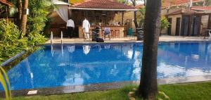 a man standing next to a swimming pool next to a house at Maggie's Guest House By NNR in Goa