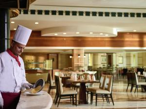 a man in a chefs hat holding a plate in a restaurant at Mövenpick Hotel Cairo - Media City in 6th Of October +43 photos
