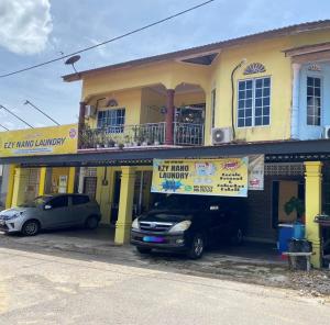two cars parked in front of a yellow building at Homestay Ezy Nano in Kampong Machang Gedibing