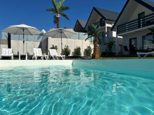 a swimming pool in front of a house with chairs and umbrellas at Sunny Baltic in Jarosławiec