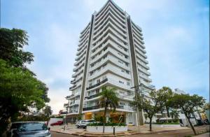 ein hohes weißes Gebäude mit davor geparkt in der Unterkunft DEPARTAMENTO EN EQUIPETROL CON PISCINA ATEMPERADA- GYM Y PARQUEO GRATIS, CERCA DEL VENTURA MALL , LOS TAJIBOS, MANZANA 40 y SUPERMERCADOS in Santa Cruz de la Sierra