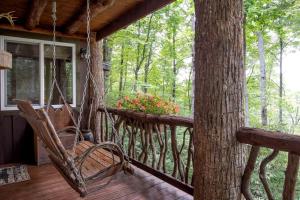 a porch with a swinging chair and a tree at Secluded Delight: Unplug and Reconnect in a Special House in Lake Toxaway's Woods in Indian Lake Estates