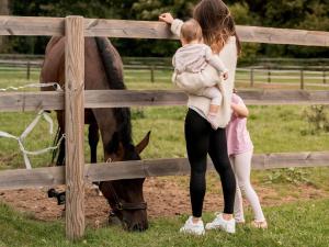 a woman holding a child looking at a horse through a fence at Hotel Novotel Domaine de Maffliers - Paris Val-d'Oise in Maffliers