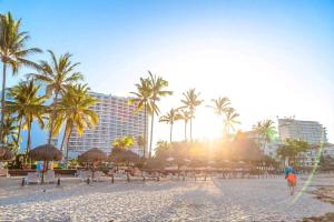 a beach with umbrellas and palm trees and a building at Ocean View 2BR Apt at Resort, 1 Block to the Beach in Puerto Vallarta