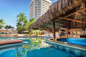 a swimming pool at a resort with a thatch roof at Ocean View 2BR Apt at Resort, 1 Block to the Beach in Puerto Vallarta