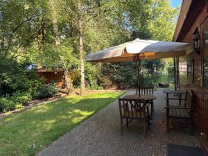 a table with an umbrella and two benches on a patio at Chaletpark de Kempenbos - 196 in Westelbeers
