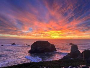 a sunset over the ocean with rocks in the water at Seaside Elegance Oceanfront Escape with 3 Suites in Bodega Bay