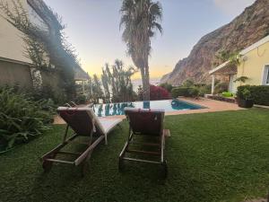 two chairs sitting in the grass near a swimming pool at Suite Bela Vigia 2 in Jardim do Mar