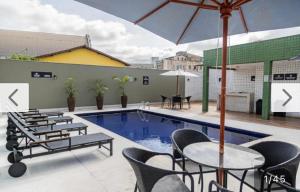 a swimming pool with tables and chairs and an umbrella at Hotel Eldorado FLAT - AP Particular 1801 in Contagem
