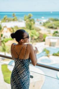 a woman standing on a balcony looking out at the ocean at Oasis Aruba Views Just for You! -Newly Refurnished in Oranjestad