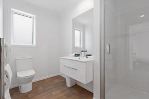 a white bathroom with a toilet and a sink at Perfect Papamoa Beach Bach in Papamoa +13 photos