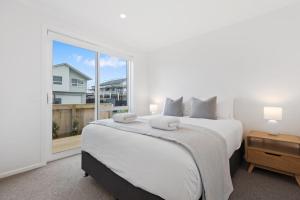 a white bedroom with a large bed and a window at Perfect Papamoa Beach Bach in Papamoa