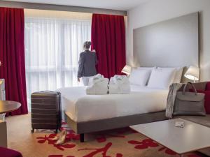 a woman standing in a hotel room with a large bed at Mercure Tours Nord in Tours