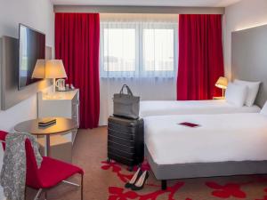 a hotel room with two beds and a desk and red curtains at Mercure Tours Nord in Tours