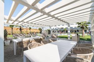 Una fila de mesas y sillas bajo una pérgola blanca. en Sea View Apartment Estepona - Célere Sea Views, en Estepona