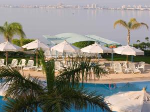 a pool with white umbrellas and chairs and a body of water at Mercure Ismailia Forsan Island in Ismailia