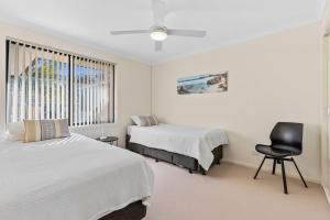 Un dormitorio con dos camas y una silla y una ventana. en Sandy Place Beach House managed by Batemans Bay Accom, en Long Beach