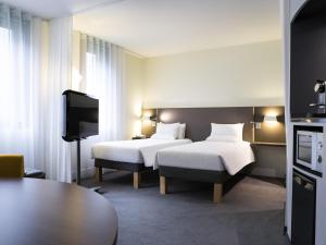 a hotel room with two beds and a tv at Novotel Suites Paris CDG Airport Villepinte in Roissy-en-France