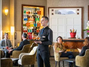 Un uomo in piedi in un bar con un vassoio di bevande di Hotel Mercure La Baule Majestic a La Baule