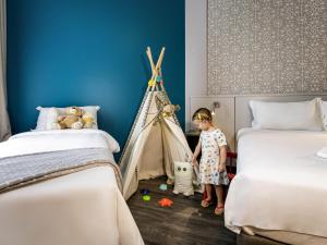 a little girl is standing between two beds at Mercure Florianópolis in Florianópolis