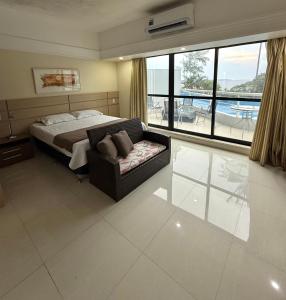 a bedroom with a bed and a couch and a large window at Hotel tropical Manaus suite luxo in Manaus