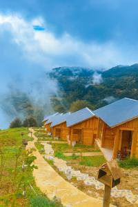 a row of wooden buildings on a hill with clouds at Samu Retreat Tà Xùa in Bắc Yên