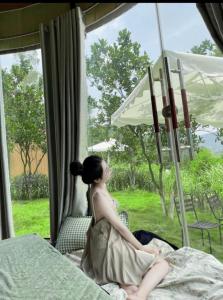 een vrouw die op een bed zit en uit een raam kijkt bij Solaria Garden Sóc Sơn in Sóc Sơn