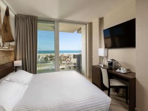 a hotel room with a bed and a desk with a window at Mercure Rimini Lungomare in Rimini