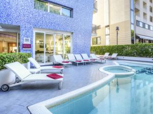 a swimming pool with lounge chairs and a building at Mercure Rimini Lungomare in Rimini