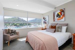 a bedroom with a bed and a chair and a large window at picton beach view apartment in Picton
