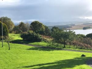 a field of green grass with a fence and a lake at Buzzard Cottage nestled in a hillside farm in Stirling