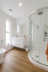 a white bathroom with a shower and a sink at Driftwood House in Foxton Beach