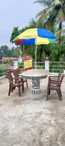 two chairs and a table with a colorful umbrella at Sandhyamalati Homestay and Picnic Ground 