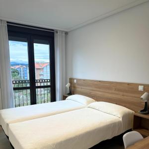 two beds in a bedroom with a large window at Apartamentos Gran Socaire de Noja in Noja
