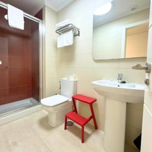a bathroom with a toilet and a sink and a red stool at Apartamentos Gran Socaire de Noja in Noja