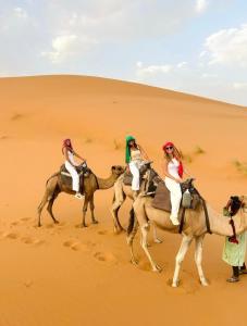 trois femmes à dos de chameau dans le désert dans l'établissement Melody Desert Camp Merzouga, à Merzouga