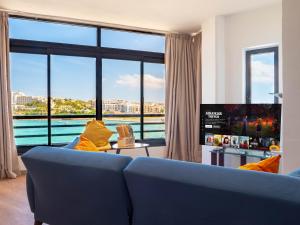 a living room with a blue couch and a large window at Shoreline Hideaway - Cross Over to the Beach! in St Paul's Bay