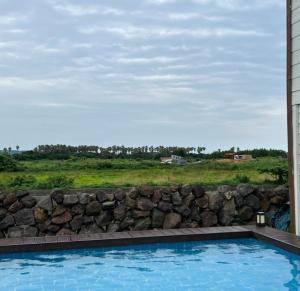 - une piscine à côté d'un mur en pierre dans l'établissement 제주 웅장한 산방산뷰 사계2248 해무리동 감성숙소, à Sagye-ri