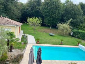 a swimming pool with two umbrellas next to a yard at Maison au vert-Entre-Deux-Mers, Repos et confort au coeur de la nature in Cursan
