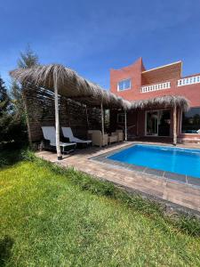 a house with a swimming pool and a straw umbrella at Villa malak in Aït Imouni