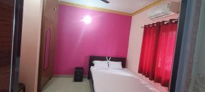 a bedroom with a pink wall with a bed and red curtains at KR HOTEL AND BANQUET Hall in Dhanbād +6 photos