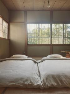 deux lits dans une chambre avec deux fenêtres dans l'établissement 森と温もりに包まれる長野飯綱高原の隠れ宿ヴァイオレットハウス, à Nagano