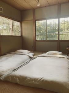 deux lits dans une chambre avec deux fenêtres dans l'établissement 森と温もりに包まれる長野飯綱高原の隠れ宿ヴァイオレットハウス, à Nagano