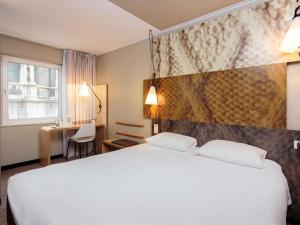 a hotel room with a white bed and a desk at Ibis Brussels City Centre in Brussels