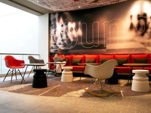 a man sitting on a red couch in a room with tables and chairs at Hotel ibis Lisboa Saldanha in Lisbon +130 photos